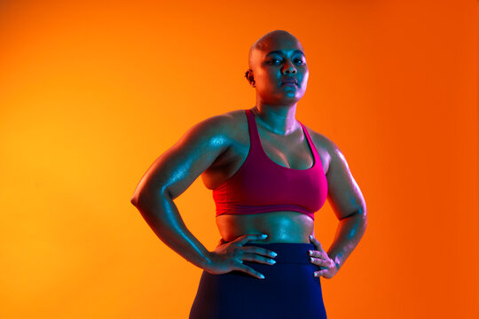 Bald athlete in sportswear posing confidently in a studio with an orange background
