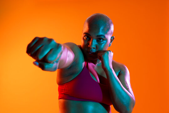 Bald athlete in sportswear punching in a studio with an orange background