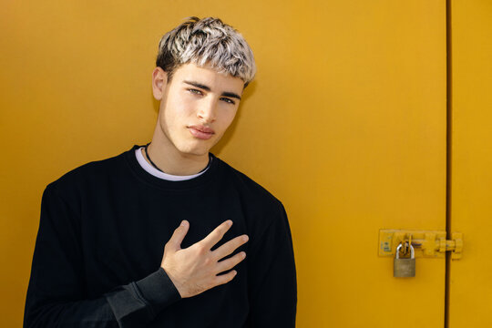Confident portrait of young man outdoors hand on chest against yellow background