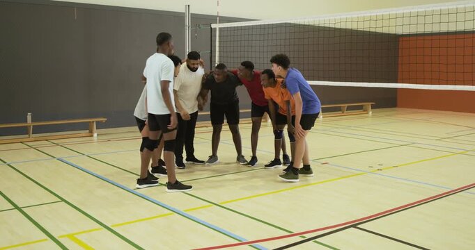 Diverse male volleyball team gathering at net for pre-play rally, aligning feet and stacking hands