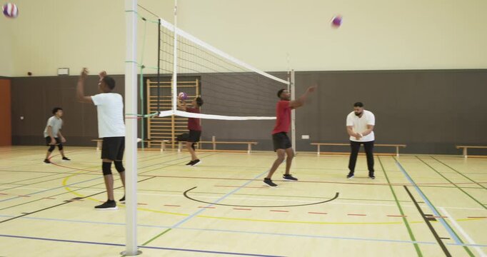 Male teammates serving, bumping, diving at gym after right toss of purple volleyball, keeping rally
