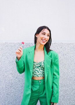 Smiling woman in green suit holding lollipop outdoors