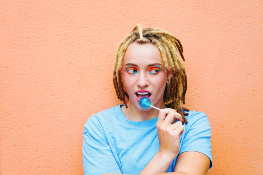 Woman with dreadlocks enjoying lollipop against orange wall