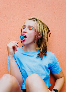 Portrait of young woman with dreadlocks and vibrant makeup enjoying a lollipop