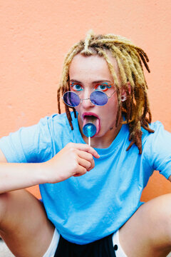 Young woman with dreadlocks and makeup enjoying lollipop in style