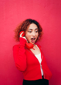 Redhead in red jacket holding telephone reacting with surprise