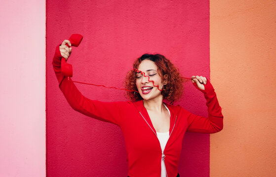 Redhead with curly hair smiling holding telephone on colorful wall