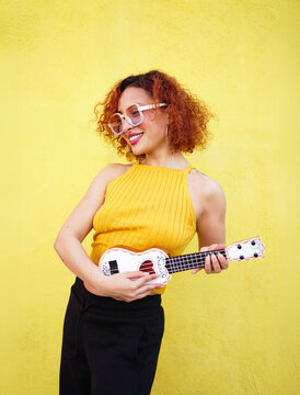 Smiling musician with ukulele in yellow top on vibrant background