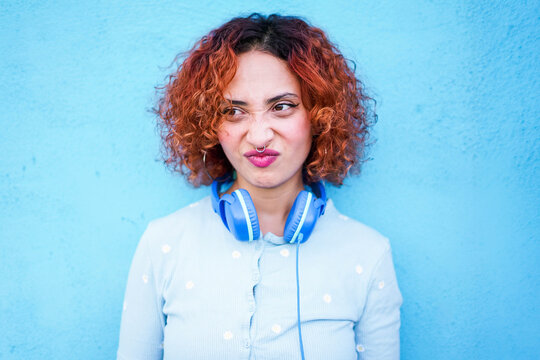 Redhead with headphones and playful expression against blue wall
