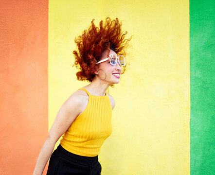 Redhead model with curly hair smiling in front of colorful wall