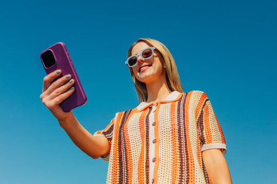 Smiling woman taking a selfie outdoors with smartphone in summer
