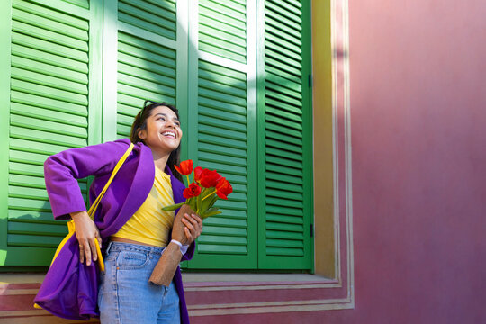 Smiling woman with tulips in front of green shuttered window outdoors