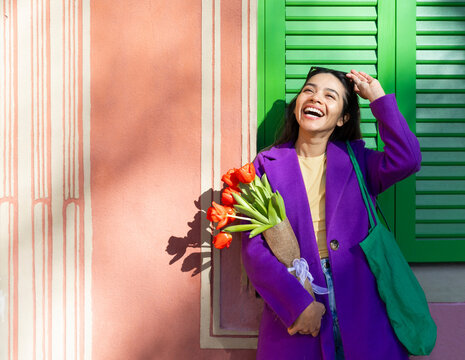 Smiling woman holding tulips in vibrant purple coat outdoors