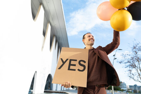Businessperson celebrating success outdoors with balloons and YES sign