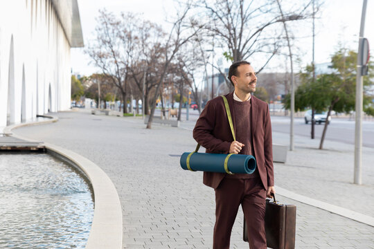 Businessman outdoors on morning commute carrying yoga mat and briefcase