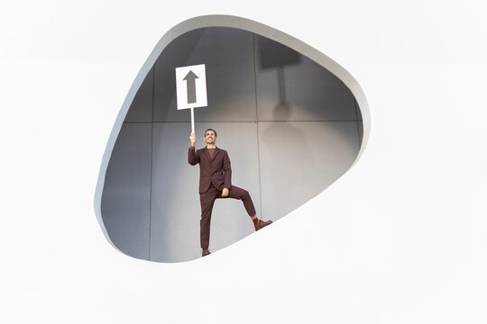 Businessman celebrating achievement holding upward arrow sign indoors