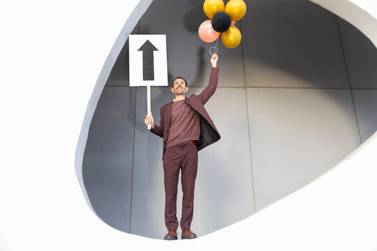 Businessman celebrating success with balloons and upward arrow sign
