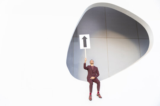 Businessman in suit holding up arrow sign celebrating career success