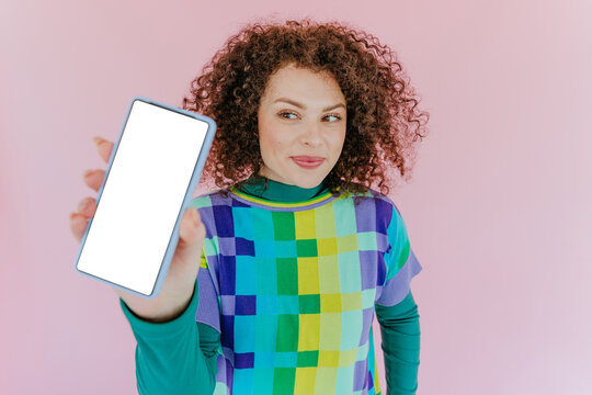 Smiling woman showing smartphone with blank screen on pink background