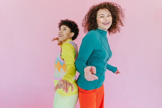 Friends dancing and smiling together against pink background