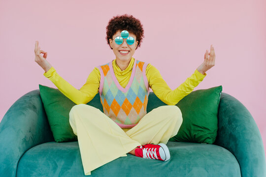Smiling woman meditating with sunglasses on pink background