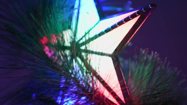 Colorful christmas star tree topper surrounded by green pine garland lights flickering