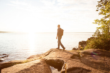Naklejka premium Hiking, travel and back with man in nature for trekking adventure, backpacking and seaside space. Walking, summer vacation and sunshine with person or hiker outdoor for ocean, explore and tourism