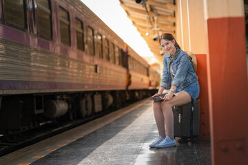 Young woman traveler using tablet while waiting at train station with suitcase, travel and...
