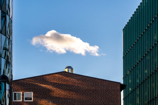 Urban building with industrial brick roof architecture under daylight sky while a bold cloud increases contrast and texture for modern city design background