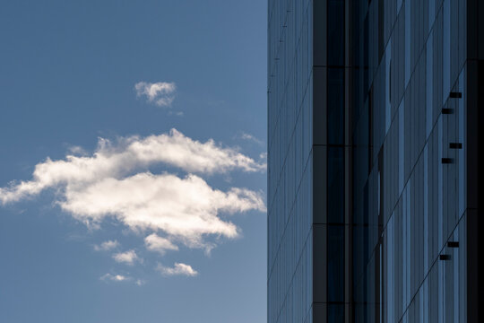 Urban building with modern glass facade architecture reaching into open sky as bright cloud adds contrast and minimal lines for clean design background