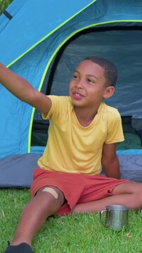 Vertical video: Reacting child when called, looking and waving at blue tent, yellow tee, cup nearby