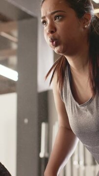 Vertical video: Pulling after inhale, woman in grey tank doing bent rows in gym with bar for power
