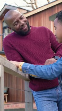 Vertical video: Talking maroon-clad father leaning on deck railing, comforting son in denim jacket