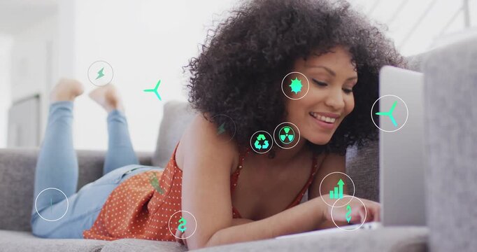 Woman lying on sofa typing on laptop, generating turquoise-green icons illustrating energy data
