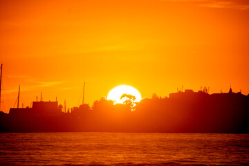 Captivating sunset scene showing the sun dipping below the horizon, illuminating the silhouetted skyline, evoking feelings of tranquility and romantic beauty. © Aperezer