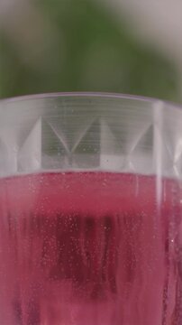 Vertical camera tilt up showing a tall glass with red fizzing drink