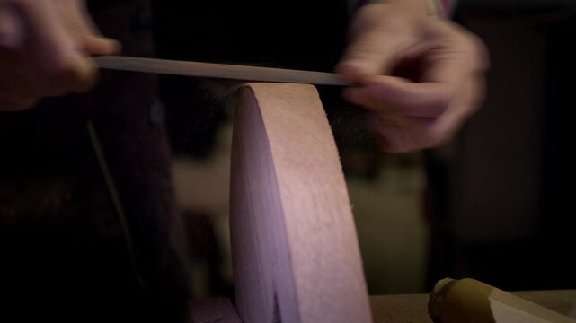 Female artisan using a metal rasp file to refine the shape and smooth the edges of a curved wooden component. Workshop scene in slow motion.