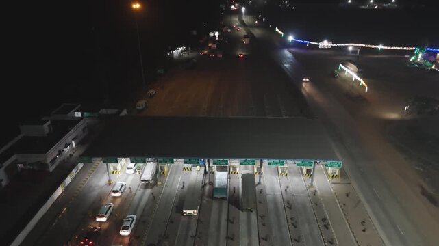 Night toll plaza with traffic lights and vehicles, Highway toll booth aerial view at night, Busy toll plaza with cars and street lights, Night traffic at toll gate on highway stock video.