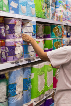 Woman household selecting paper towels from a supermarket shelf.