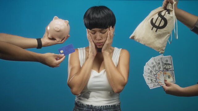 Woman holding face with hands, surrounded by cash, creditcard and piggybank in studio; financial worry.