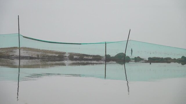 Sea-scape with mirroring images. Bottom-mounted seine nets in tidal shallow water. Foggy landscape during monsoon season. Gulf of Tonkin, Vietnam