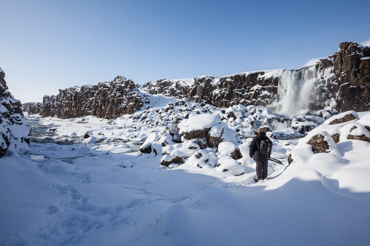 Photographer stands in the snow beside &Ouml;xar&aacute;rfoss waterfall in South Eastern Iceland