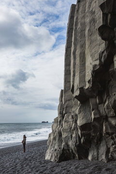 Tourist standing on Reynisfjara beach at the base of tall basalt columns looking out to sea, Iceland