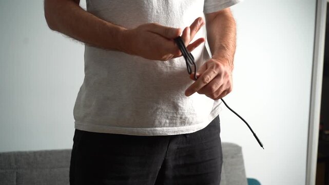 Detail shot of male hands carefully winding up a black usb cable for tidy storage and organization