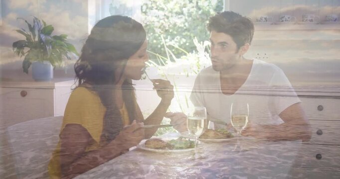 Woman cutting food, man reaching and glancing during meal, seascape overlay aiding food marketing