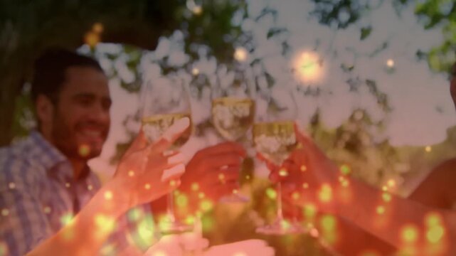Cam pulling back revealing four adults toasting glasses marking food event under tree with sparkles