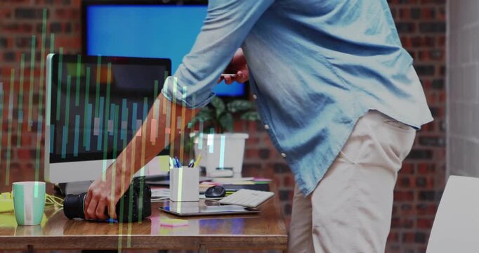 Vertical video: Entering man in blue shirt placing phone and DSLR at loft desk to edit, copy space