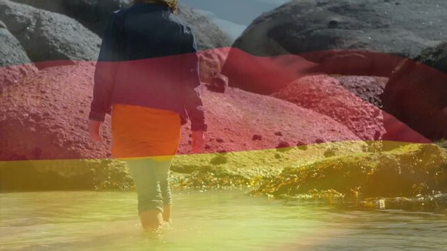 Vertical video: Clip start showing woman in sunhat orange skirt wading toward rocks with bands