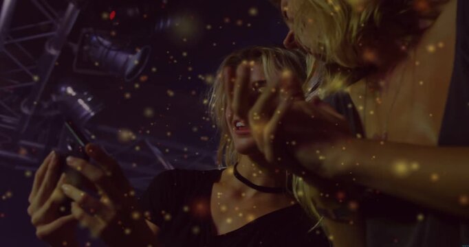 Vertical video: Women leaning to phone tapping showing concert reacting gold drifting across faces