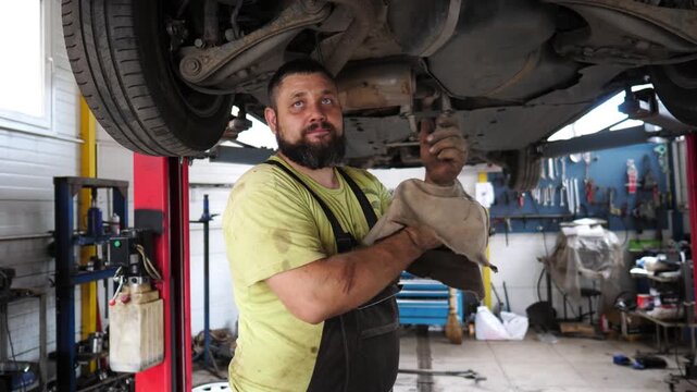 Skilled automotive mechanic performing detailed undercarriage inspection and repair on vehicle, showcasing precision and expertise in well-equipped garage environment with tools and equipment visible